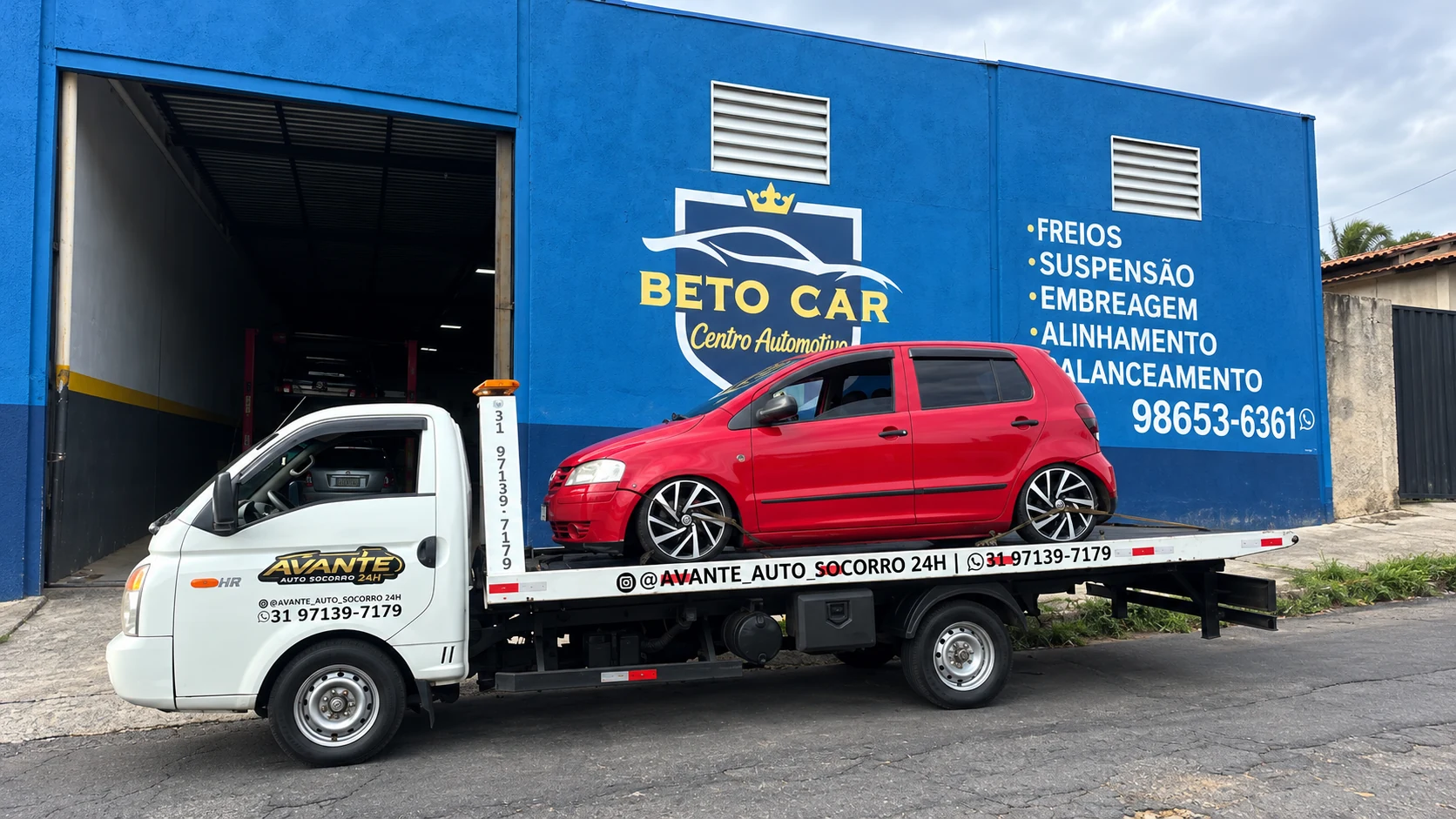 Guincho plataforma da Avante transportando um carro vermelho em frente a uma oficina.